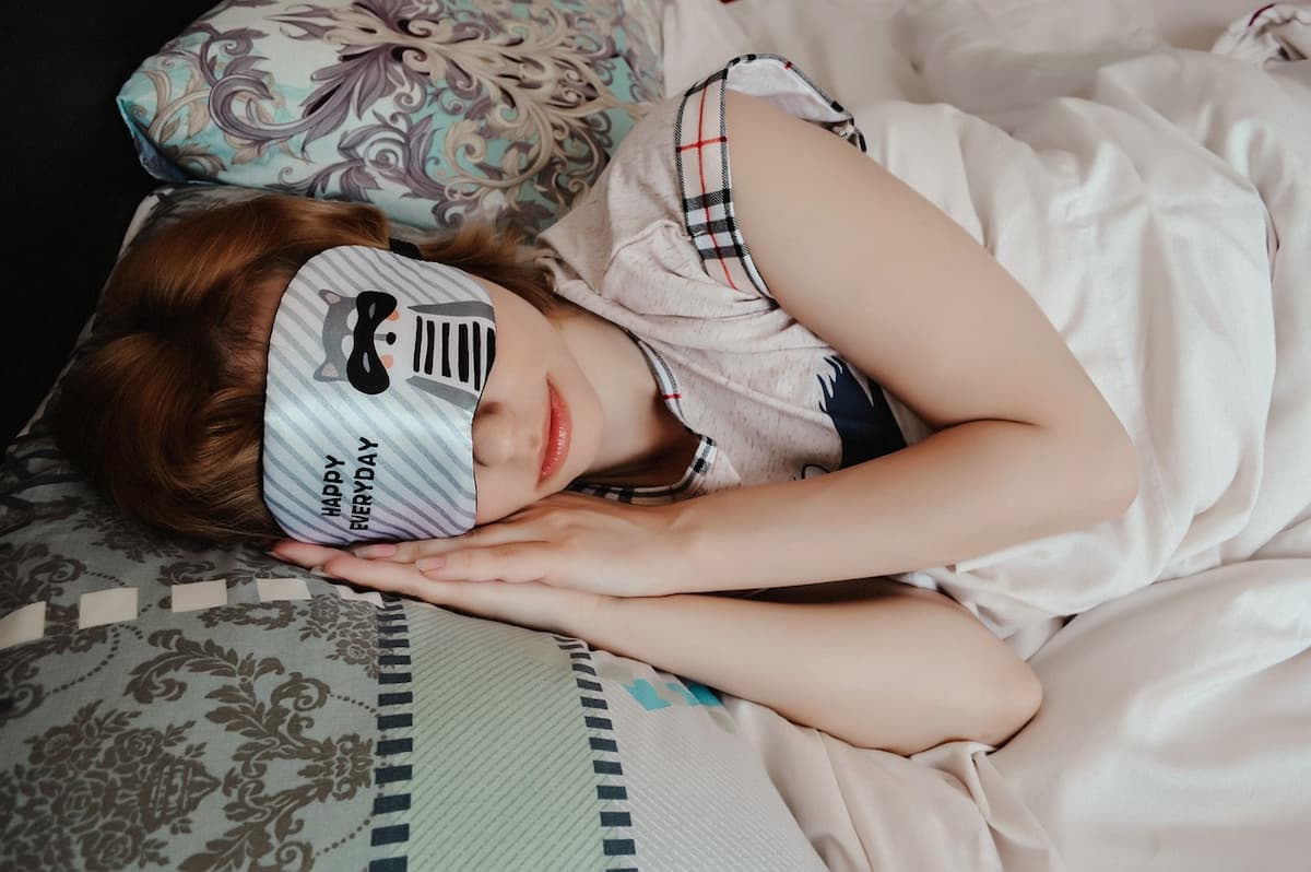 Femme dormant dans son lit en pyjama avec un cache-yeux sur le visage