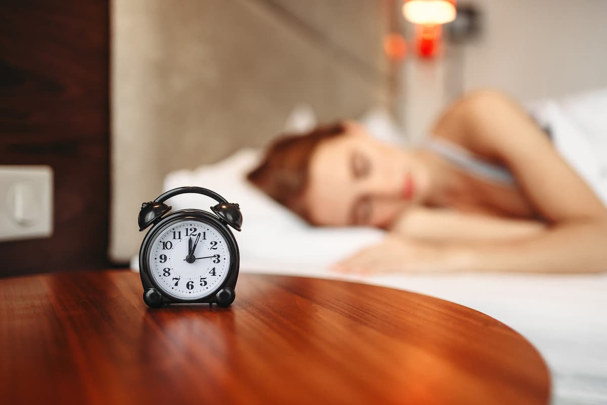 Réveil posé sur la table de nuit d'une femme endormie dans son lit